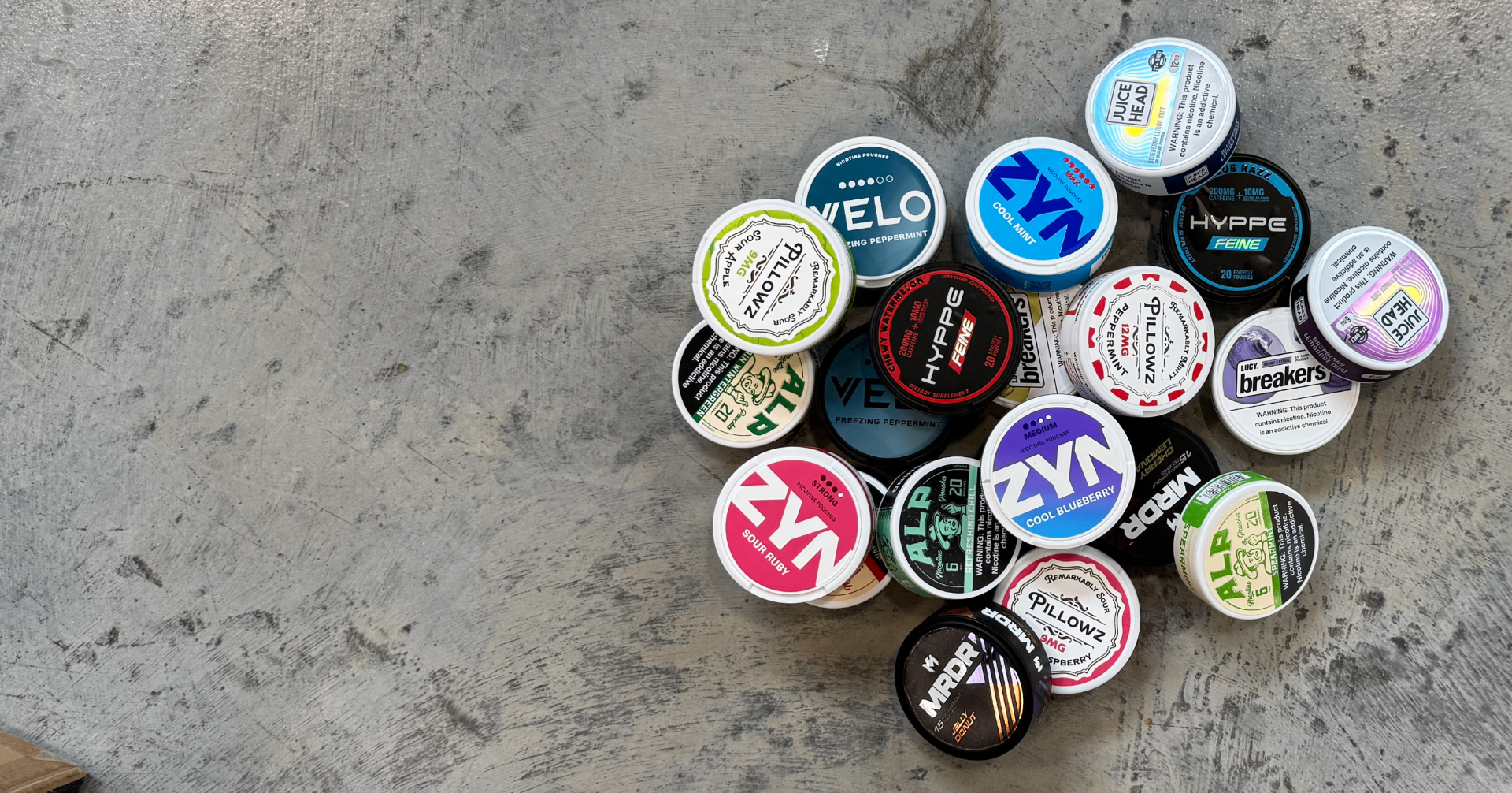 Assortment of nicotine, energy, and caffeine pouch tins clustered on a weathered concrete surface